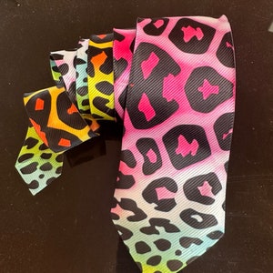 Puede incluir: Una corbata colorida con un estampado de leopardo. La corbata está hecha de una tela suave y sedosa y tiene un degradado de colores, incluyendo rosa, amarillo, verde y azul.