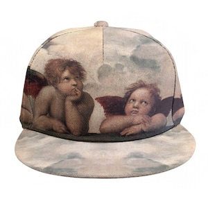 Puede incluir: Gorra de béisbol con visera plana que presenta una pintura de estilo renacentista de querubines en un cielo nublado. La gorra tiene un fondo beige claro con la obra de arte que envuelve la corona y la visera.