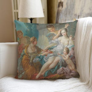 Puede incluir: Cojín cuadrado con una pintura clásica con figuras en colores pastel. La obra de arte representa a varias personas en un jardín, con un enfoque en azules, amarillos y rosas suaves. El cojín está colocado sobre un sofá blanco.