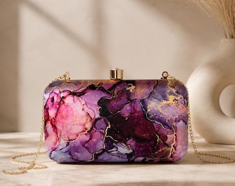 Pochette in raso con stampa effetto marmo astratto e cornice dorata, tracolla a catena removibile.