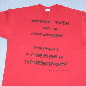 May include: Red t-shirt with black text that reads "never talk to a stranger cause I could be a heartbreaker" and a website address at the bottom.