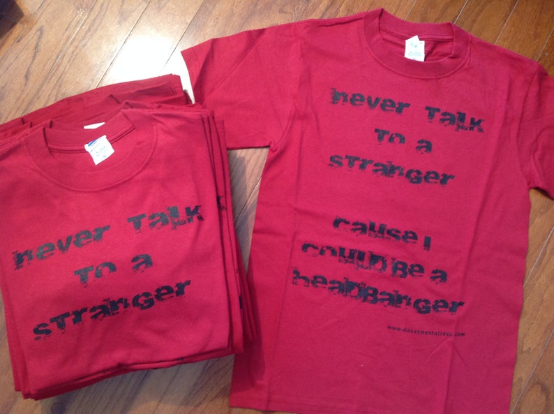 May include: Two red t-shirts with black text. The text on the top shirt reads "never talk to a stranger cause I could be a heartbreaker". The text on the bottom shirt reads "never talk to a stranger".