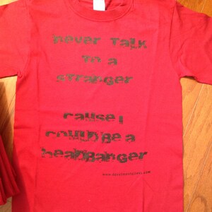 May include: Red t-shirt with black text that reads "never talk to a stranger cause I could be a heartbreaker" and a website address at the bottom.