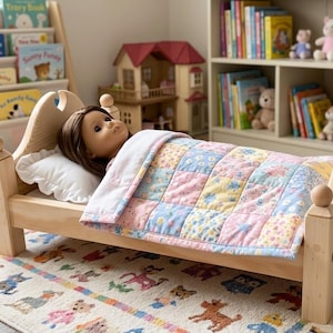 May include: A wooden doll bed with a light natural finish, featuring a doll with brown hair resting on a white pillow. The bed is covered by a patchwork quilt in pastel shades of pink, blue, and yellow with a floral and star pattern design.