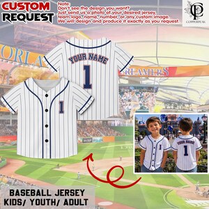 Puede incluir: Una camiseta de b&eacute;isbol blanca con finas rayas verticales azul marino, cierre de botones y ribetes azul marino. La camiseta presenta el texto YOUR NAME y el n&uacute;mero 1 en azul marino con un borde rojo en la parte posterior y en el pecho.