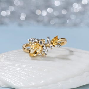 May include: A gold ring featuring two insect-shaped motifs adorned with oval-cut yellow citrine gemstones and small round white diamonds. The design includes a larger insect on the left and a smaller one on the right, set in polished yellow gold.
