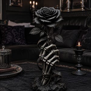 May include: A decorative sculpture featuring a detailed skeletal hand grasping the stem of a single, large black rose. The hand and rose are mounted on a textured, dark base, showcasing intricate bone structures and layered rose petals in monochromatic tones.