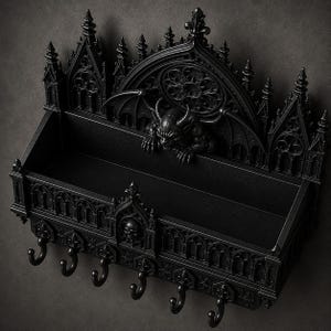 Puede incluir: Un estante de pared negro que presenta una figura central de gárgola con alas, detalles arquitectónicos góticos intrincados que incluyen arcos apuntados y un diseño de rosetón, y seis ganchos metálicos curvos en el borde inferior.
