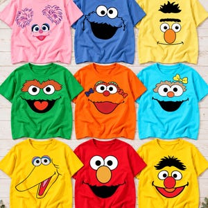 May include: A collection of nine short-sleeved t-shirts in various colors, each featuring a graphic print of a Sesame Street character face, including Abby Cadabby, Cookie Monster, Bert, Oscar the Grouch, Zoe, Rosita, Big Bird, Elmo, and Ernie.