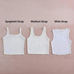 May include: Three white crop tops arranged side by side. The first is labeled Spaghetti Strap, the second is labeled Medium Strap, and the third is labeled Wide Strap. Each top features a different shoulder strap width and a scoop neckline.