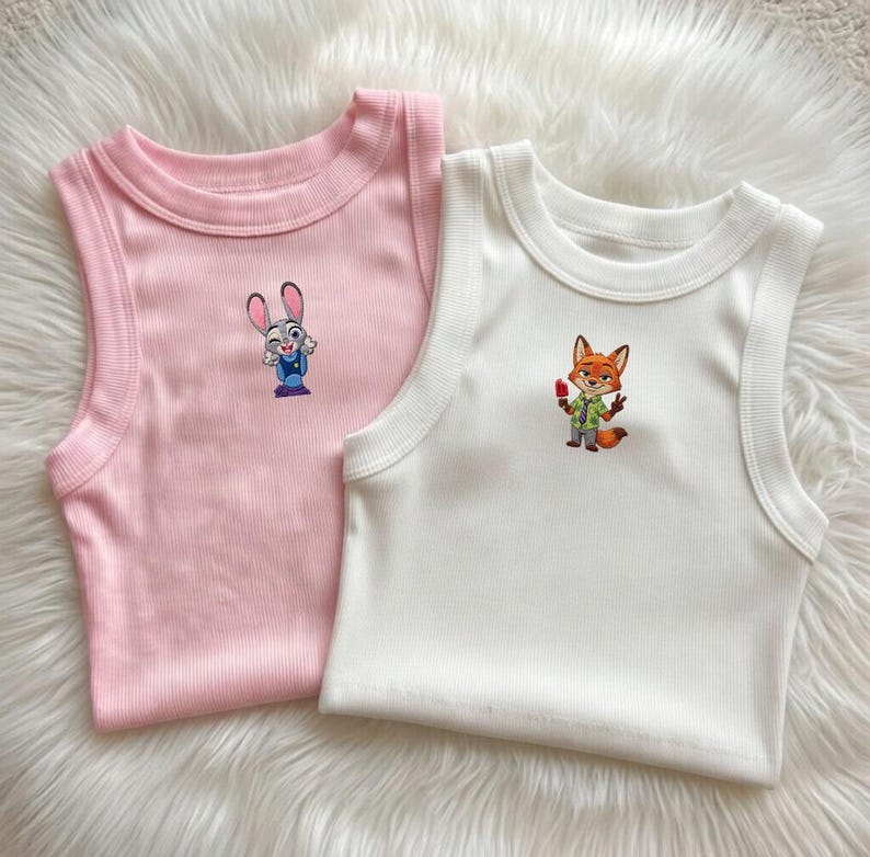 May include: Two ribbed tank tops, one light pink and one white, each featuring a small embroidered character on the chest. The pink tank displays a grey rabbit character, while the white tank features an orange fox character holding a red popsicle.
