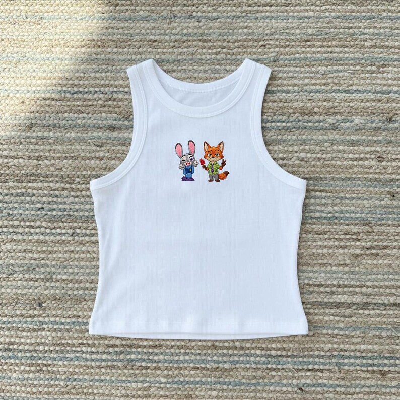 May include: A white sleeveless ribbed tank top featuring a small, centered graphic print of a cartoon rabbit and a cartoon fox standing side by side. The rabbit has grey fur and a blue uniform, while the fox has orange fur, a green shirt, and a tie.
