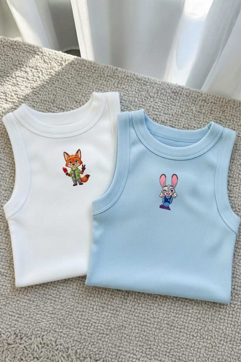 May include: A white ribbed tank top featuring an embroidered orange fox character holding a red popsicle and a light blue ribbed tank top featuring an embroidered grey rabbit character with large ears and a blue uniform, both with crew necklines.