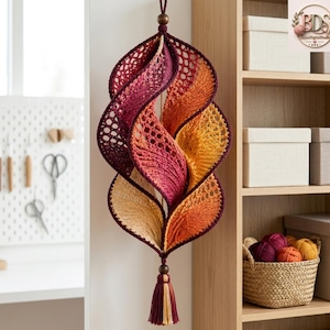 K&ouml;nnte beinhalten: Eine h&auml;ngende H&auml;keldekoration mit einem Spiraldesign und einem Farbverlauf von Dunkelviolett und Magenta bis hin zu leuchtendem Orange und Gelb. Das St&uuml;ck ist oben mit einer dunkelbraunen Holzperle und unten mit einer passenden Quaste versehen.