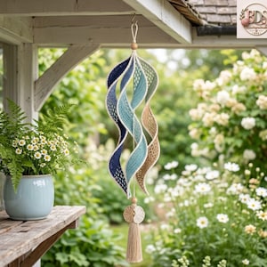 May include: A hanging spiral wind spinner made of crocheted yarn in a gradient of dark blue, light blue, and beige. The structure features a central cord with wooden beads at the top and bottom, finished with a beige tassel at the lower end.