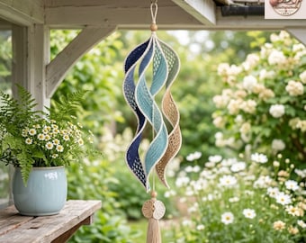 Könnte beinhalten: Ein hängendes Spiral-Windspiel aus gehäkeltem Garn in einem Farbverlauf von Dunkelblau, Hellblau und Beige. Die Struktur besteht aus einer mittigen Schnur mit Holzperlen oben und unten, abgeschlossen mit einer beigen Quaste am unteren Ende.