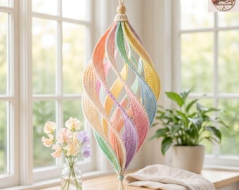 Könnte beinhalten: Ein hängendes Spiralornament aus gehäkelten Stoffstreifen in Pastelltönen wie Pfirsich, Minzgrün, Gelb, Blau und Lavendel. Die Struktur verfügt über eine zentrale Holzperle an der Oberseite und eine kleine Quaste an der Unterseite, aufgehängt an einer Kordel.