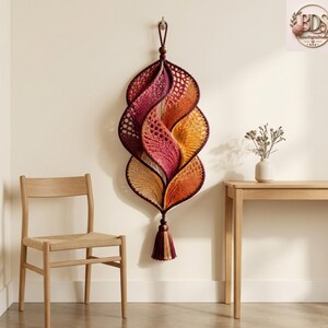 K&ouml;nnte beinhalten: Ein vertikaler Wandbehang mit einem Spiralmuster aus geh&auml;keltem Garn in einem Farbverlauf von Dunkelviolett, Magenta, Orange und Creme. Das St&uuml;ck ist an einer Holzperle aufgeh&auml;ngt und mit einer passenden, mehrfarbigen Garnquaste versehen.
