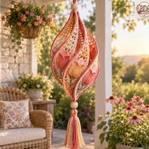 May include: A hanging crochet ornament featuring a spiral design with integrated tulip motifs in shades of coral, peach, and yellow. The piece is accented with a wooden bead at the top and bottom, and it terminates in a multi-colored yarn tassel.