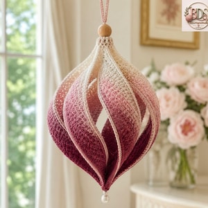May include: A hanging crochet ornament featuring a spiraling, teardrop-shaped design. The yarn transitions in color from a light cream at the top to a deep burgundy at the bottom. A small wooden bead sits at the top, and a white pearl bead hangs below.