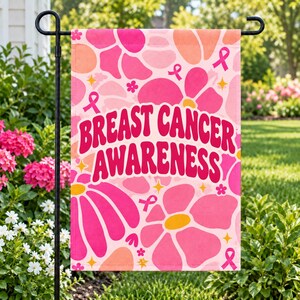 May include: A rectangular garden flag featuring a pink and orange floral pattern with breast cancer awareness ribbons and yellow star accents. The text BREAST CANCER AWARENESS is printed in a bold, dark pink, retro-style font across the center.