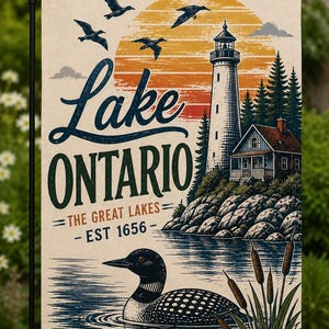 May include: A rectangular garden flag featuring a graphic illustration of a lighthouse, a cabin, and a loon on water. The text reads Lake ONTARIO THE GREAT LAKES EST 1656. The scene includes a large orange sun, flying birds, and cattails.