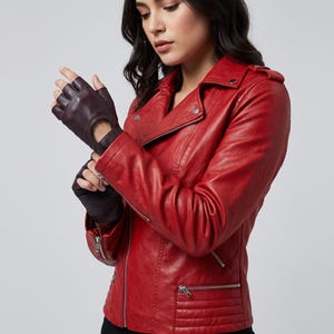 Peut inclure: Une veste de moto rouge vif avec des fermetures éclair argentées, des boutons-pression sur les revers et des détails matelassés à la taille, associée à des gants en cuir marron foncé sans doigts avec une découpe sur le dos de la main.