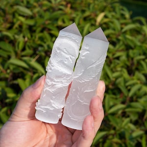 May include: Two translucent white crystal towers with pointed tops. One tower features a detailed relief carving of a coiled dragon, while the other displays a relief carving of a phoenix with wings spread. Both pieces have a smooth, frosted texture.