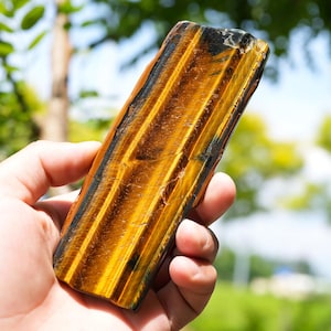 May include: A rectangular slab of polished tiger's eye gemstone featuring alternating vertical bands of golden yellow and deep black. The stone displays a chatoyant, silky luster with a smooth, flat surface and defined, straight edges.