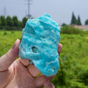 以下が含まれることがあります： 鮮やかなターコイズブルーのヘミモルファイト鉱物標本。研磨されていない原石で、結晶質の表面は非常に質感が高く、自然な亀裂や不規則な形状が見られます。全体に鮮やかで彩度の高い青色が広がっています。