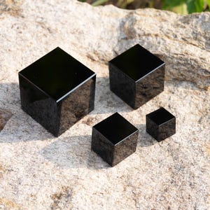 May include: A set of four solid black cubes of varying sizes, each featuring a smooth, reflective surface and sharp, defined edges. The cubes are arranged in a cluster, showcasing a consistent geometric form with a deep, uniform black colour.