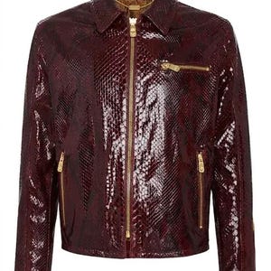 Puede incluir: Una chaqueta de color burdeos oscuro con un patrón de piel de serpiente brillante y texturizado. La prenda incluye un cuello puntiagudo, una cremallera central dorada, un bolsillo en el pecho, dos bolsillos laterales y cremalleras en las mangas.
