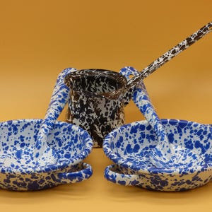 May include: Two white enamel bowls with blue speckled patterns, each featuring two side handles and a matching blue speckled ladle. A central white enamel pitcher with a black speckled pattern and a long handle sits behind the two bowls.