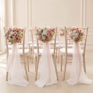 Puede incluir: Un conjunto de sillas de madera de color claro, cada una con un respaldo redondeado adornado con un gran arreglo floral de rosas rosas y blancas y paniculata, complementado con un largo y fluido drapeado de tela blanca transparente.
