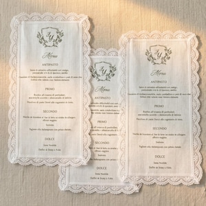 May include: Three rectangular white fabric menus with scalloped lace borders. Each menu features a printed crest with the initials JY at the top, followed by the word Menu and sections for Antipasto, Primo, Secondo, and Dolce with printed text.