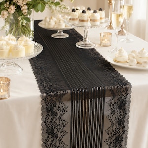 May include: A black lace table runner featuring a central panel of vertical stripes flanked by intricate floral lace borders with scalloped edges, draped over a white tablecloth and surrounded by various desserts and glassware.