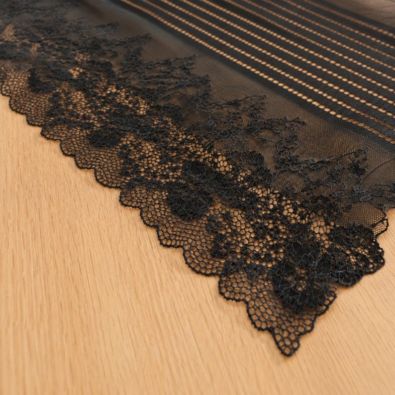 May include: A black sheer fabric featuring a wide, intricate floral lace border with a scalloped edge. The upper section of the fabric displays a pattern of thin, vertical stripes composed of small, delicate dots on a translucent mesh base.