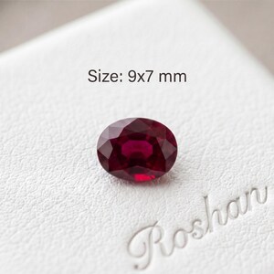 May include: A deep red, oval-cut gemstone with a faceted surface. The stone is positioned above the text "Roshan" and below the text "Size: 9x7 mm", indicating its dimensions. The gemstone displays a rich, saturated crimson color throughout.