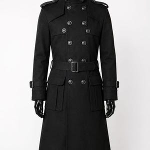 May include: A black double-breasted trench coat featuring a high collar with buckle straps, shoulder epaulets, and a waist belt with a rectangular buckle. The coat includes two large front flap pockets and adjustable buckle straps on the cuffs.