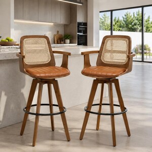 May include: Two swivel bar stools featuring dark wood frames, tan faux leather upholstered seats with horizontal stitching, and light-colored woven cane backrests. Each stool includes curved armrests and a circular black metal footrest ring.