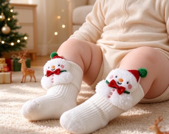 Può includere: Un paio di calzini in maglia a coste bianchi con applicazioni di pupazzi di neve in peluche sui polsini. Ogni pupazzo di neve ha un papillon rosso, un cappello rosso con un pompon verde, un naso a carota arancione e guance rosa.