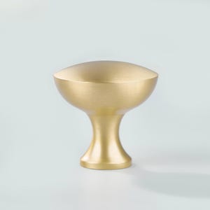 May include: A cabinet knob with a brushed gold finish, featuring a wide, rounded top that tapers down to a narrow, circular base. The hardware has a smooth, metallic texture and a consistent, soft golden color throughout its entire structure.