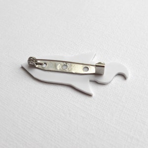 May include: White rocket ship shaped pin with a silver metal pin back.