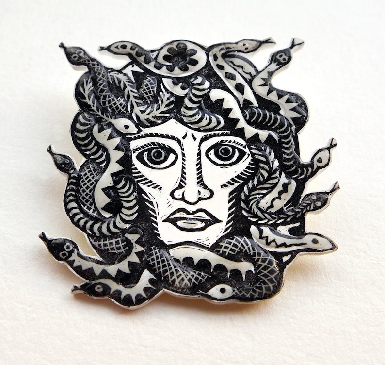 May include: Black and white illustration of Medusa, a mythical Greek figure with snakes for hair, depicted as a woman's face with a crown of snakes.