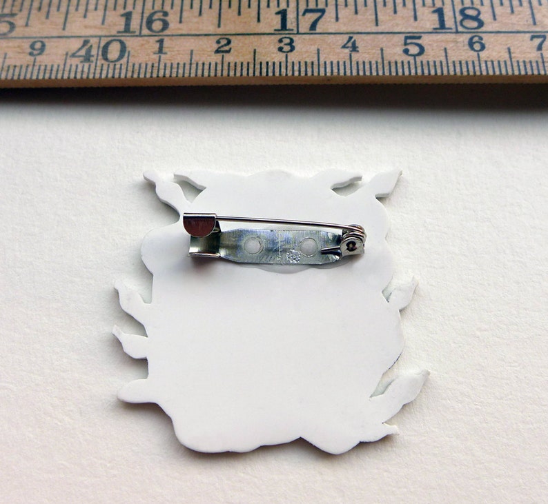 May include: White ceramic pin with a detailed design of a creature with a pin back.