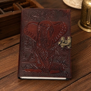 May include: A dark brown leather journal featuring an embossed elephant design on the front cover. The notebook is secured with a vintage-style brass metal latch closure. The cover texture includes intricate floral and foliage patterns.