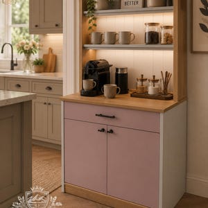 May include: A wooden coffee station cabinet featuring a light pink two-door base with a drawer, a natural wood countertop, and two open shelves with integrated lighting. The shelves hold mugs, glass jars, and a sign reading COFFEE MAKES EVERYTHING BETTER.