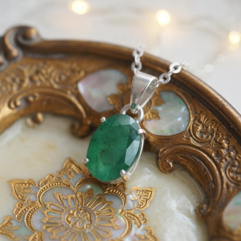 Elegant 10–15Ct Emerald Pendant Necklace featuring a natural green emerald in a classic oval cut. The gemstone displays beautiful natural variations and subtle light reflections that emphasize its authentic character. Set against a delicate silver-tone chain, this minimalist May birthstone necklace makes a versatile accessory for casual and formal fashion and a thoughtful gift for women, gemstone collectors, May birthdays, and emerald jewelry enthusiasts.