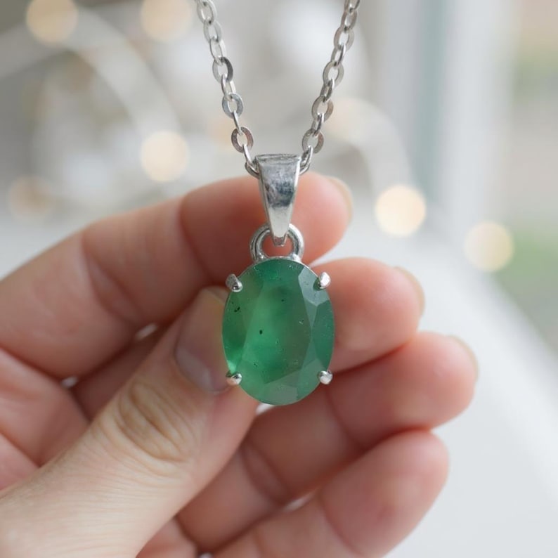 Dainty Green Emerald Necklace featuring a 10–15Ct natural oval-cut emerald pendant with a rich green appearance and natural gemstone characteristics. The elegant pendant is displayed on a delicate silver-tone chain, creating a refined minimalist jewelry style. This May birthstone necklace is perfect for everyday wear, office outfits, dinners, weddings, parties, anniversaries, birthdays, and special occasions, making it a thoughtful gemstone jewelry gift for women and emerald lovers.
