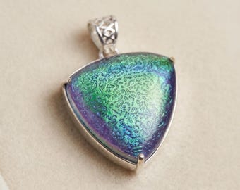 May include: A triangular pendant featuring a vibrant, iridescent glass surface with a textured, crackled pattern in shades of shimmering green and deep purple, set within a polished silver-toned metal frame with a decorative filigree bail.